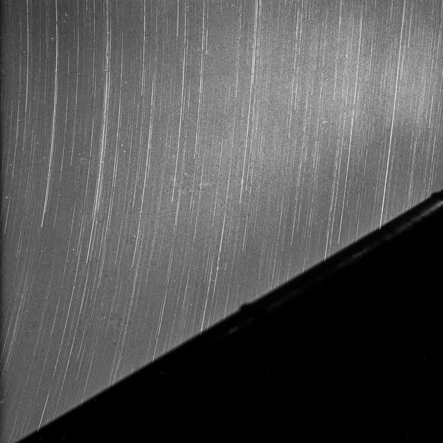 Vertical star trails above a rooftop, in black and white