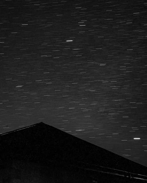 Star trails above a triangular rooftop, in black and white